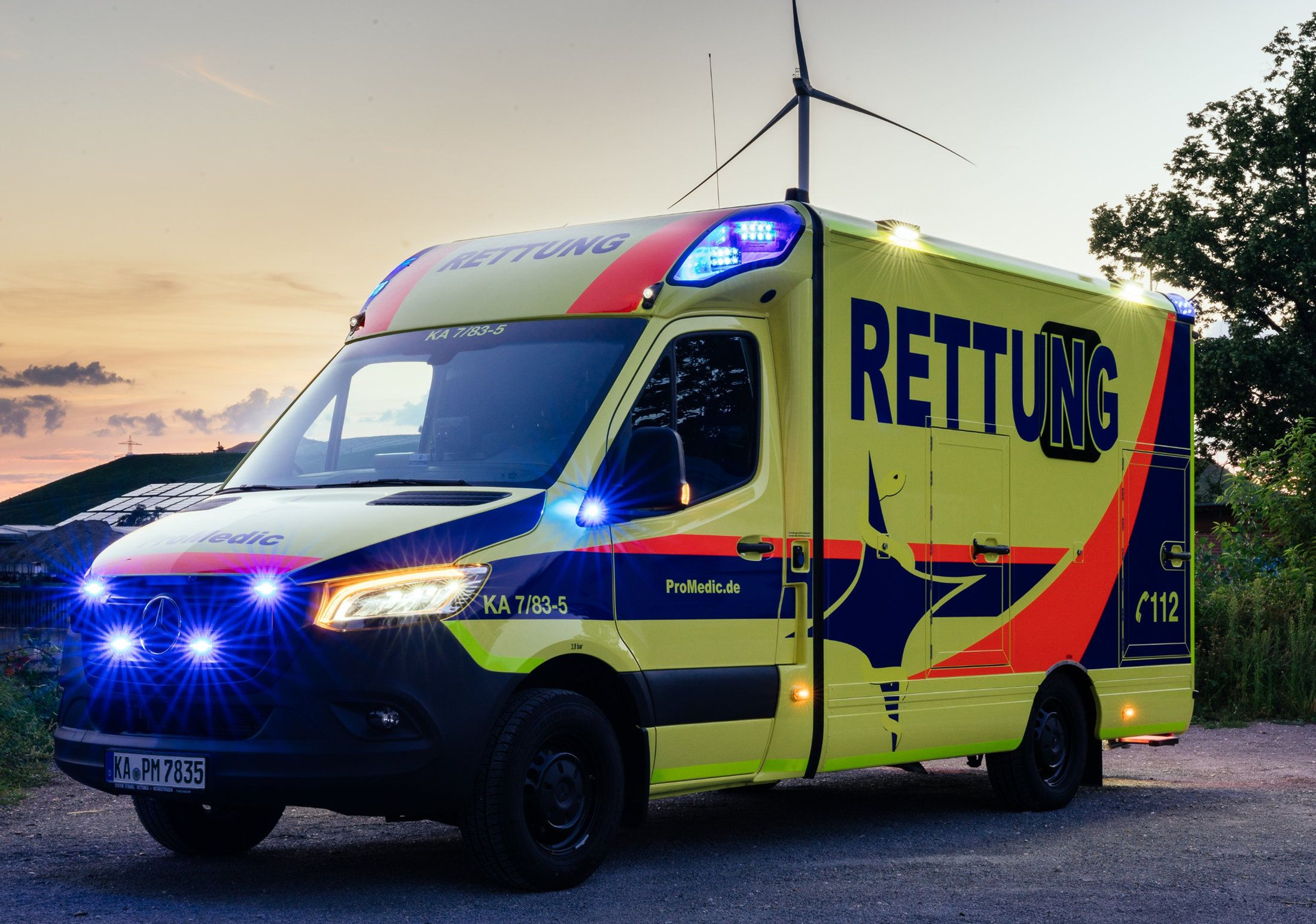 ProMedic-Rettungswagen in Leuchtgelb mit eingeschaltetem Blaulicht in der Abenddämmerung